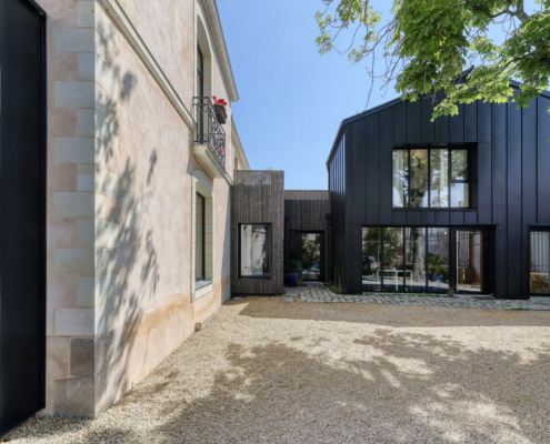 Cour intérieure : liaison en bardage bois clair entre la maison ancienne en pierre et l'extension en bardage zinc noir