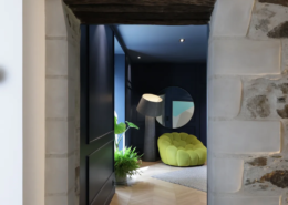 Entrée en pierre ancienne avec poutre bois apparente, ouvrant sur le salon aux murs bleu nuit