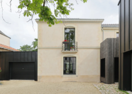 Façade principale de la maison bourgeoise en pierre et enduit clair, avec garage habillé de zinc noir