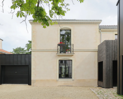 Façade principale de la maison bourgeoise en pierre et enduit clair, avec garage habillé de zinc noir