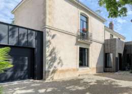 Façade principale de la maison bourgeoise en pierre et enduit clair, avec garage habillé de zinc noir