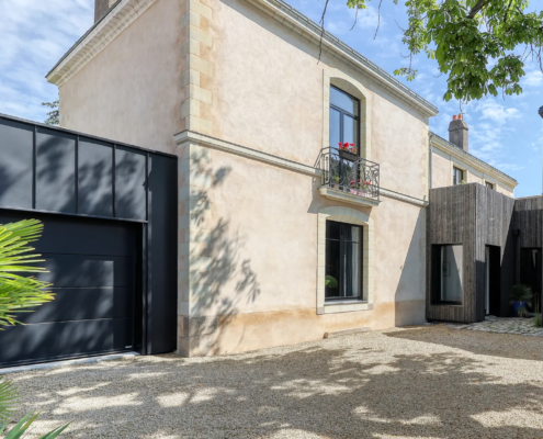 Façade principale de la maison bourgeoise en pierre et enduit clair, avec garage habillé de zinc noir