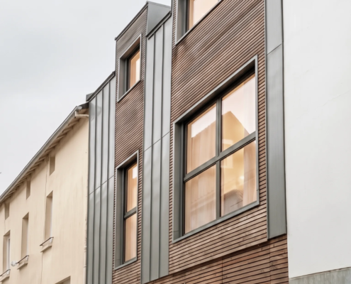 Perspective de la façade en bardage bois agricole et zinc depuis la ruelle, maison au Pellerin (44)