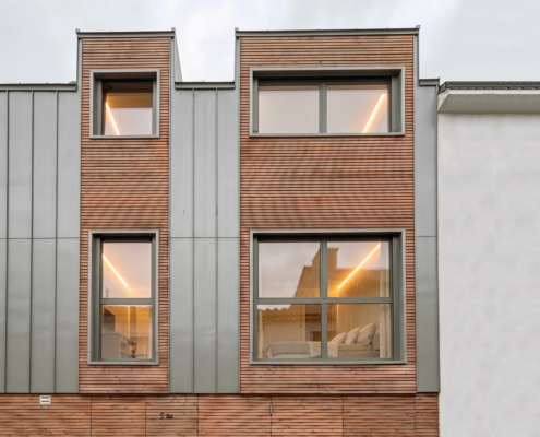 Vue rapprochée de la façade en bardage bois agricole et zinc, insérée dans une ruelle étroite au Pellerin