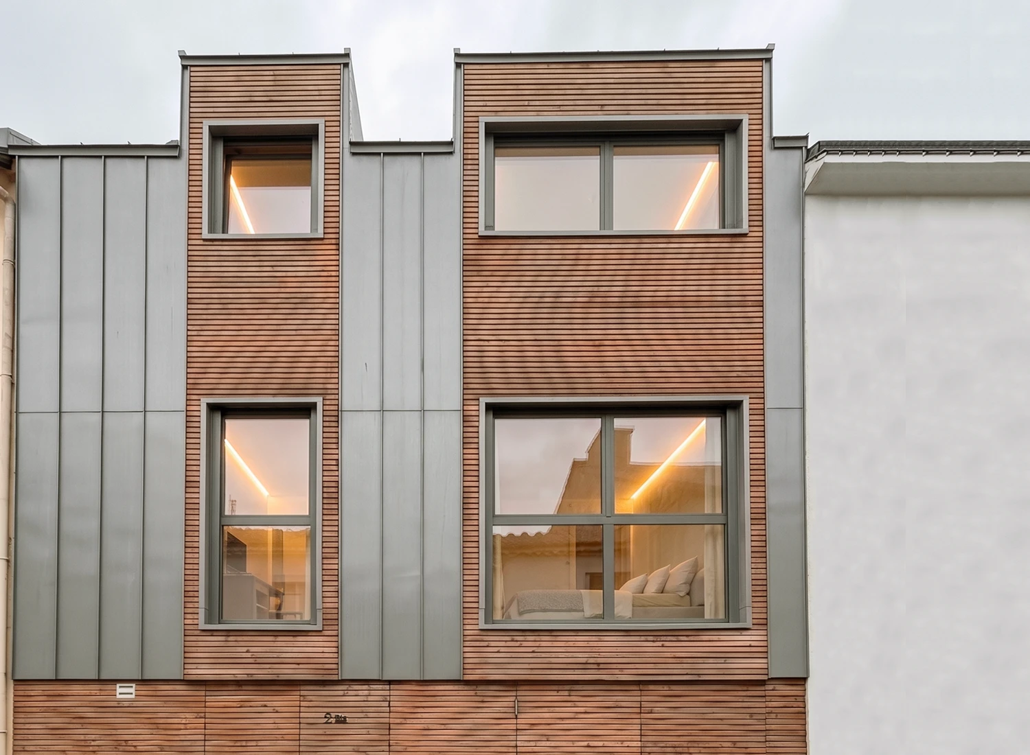 Vue rapprochée de la façade en bardage bois agricole et zinc, insérée dans une ruelle étroite au Pellerin